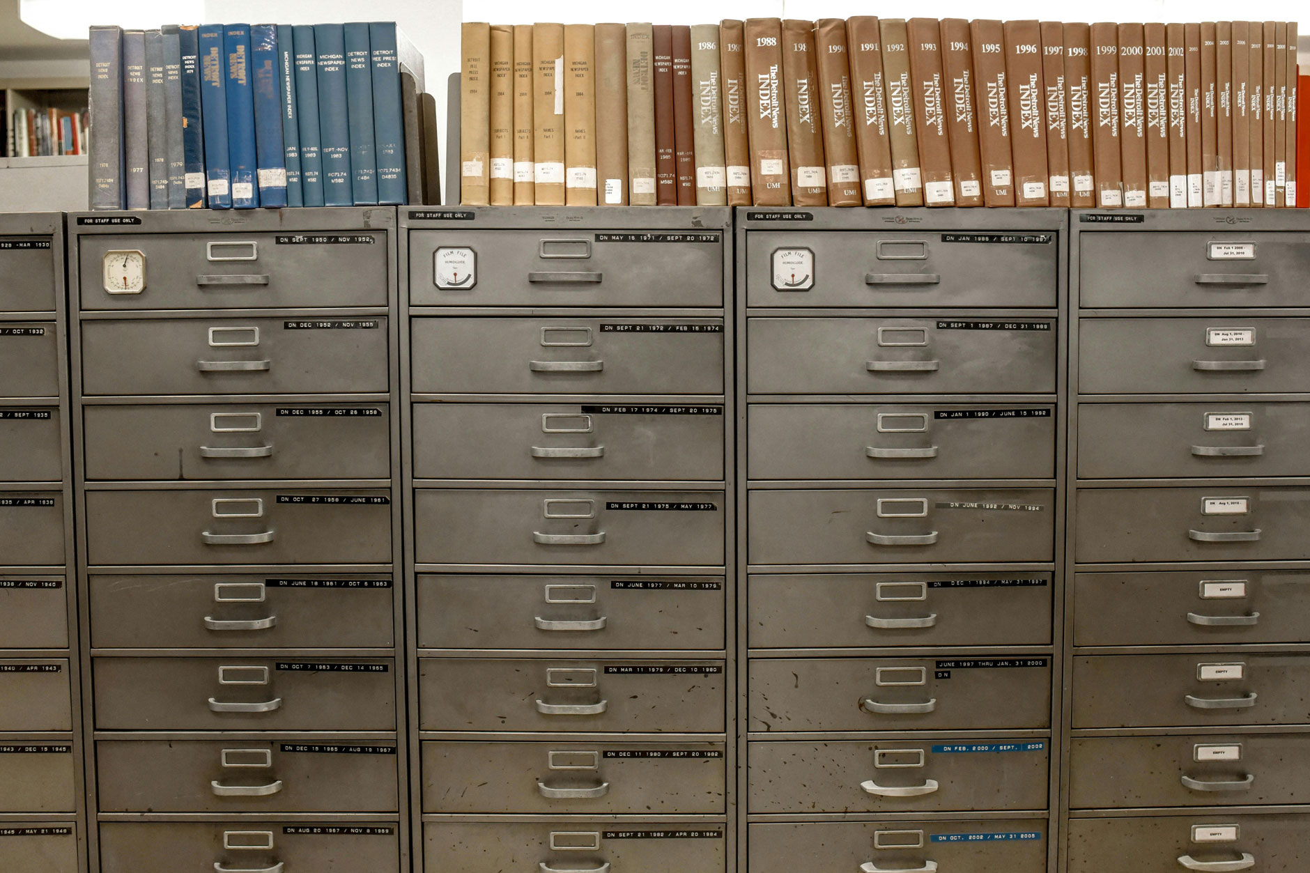 Three metal filing cabinets with multiple drawers stand side by side, topped with neatly arranged books and two small clocks.