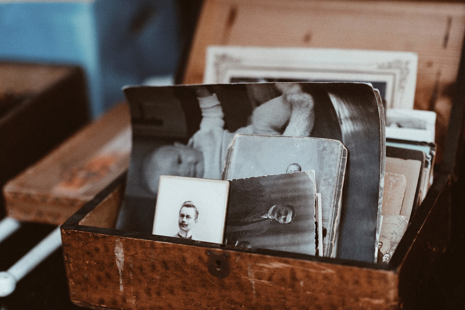 An open wooden box filled with old black-and-white photos, some slightly bent, sits on a table.