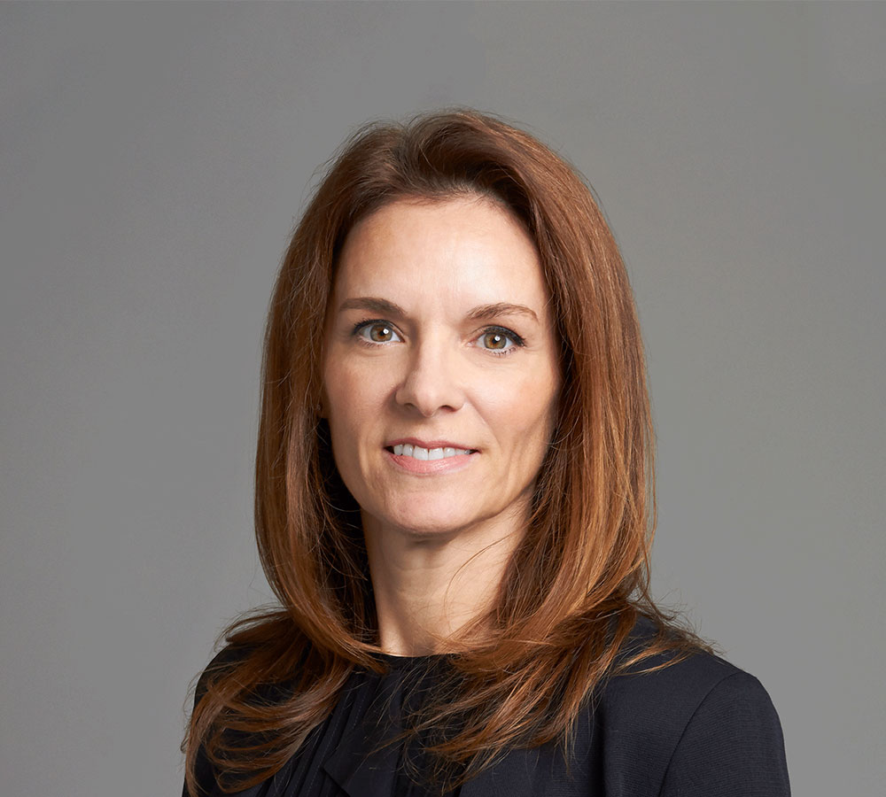 A woman with brown hair and a black shirt smiles at the camera against a plain background.