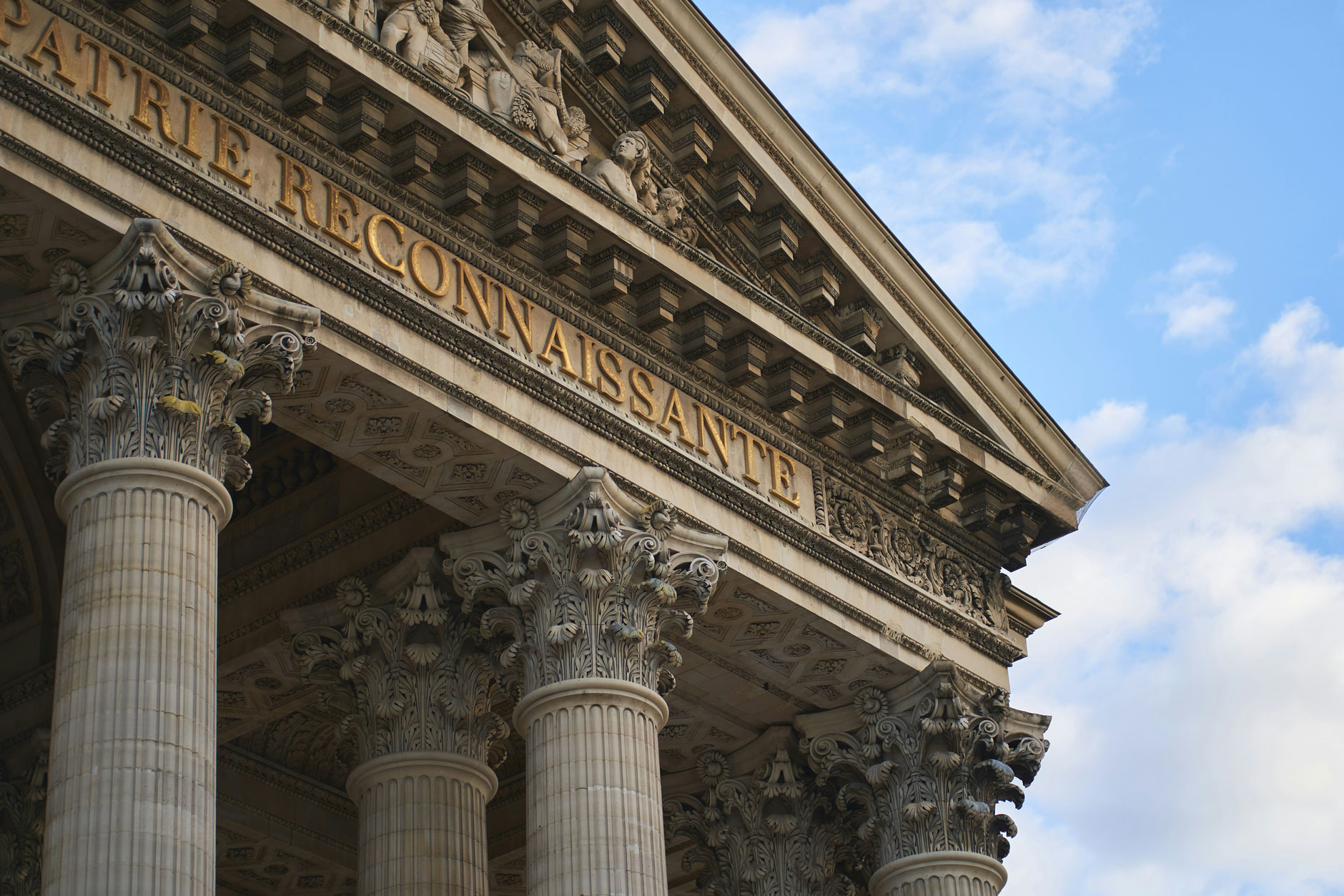 Close-up of ornate Corinthian columns and carvings on a classical facade with "LA PATRIE RECONNAISSANTE" inscription.