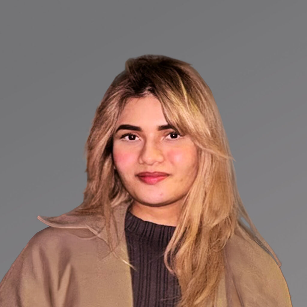 A young woman with long blonde hair and a slight smile wears a taupe jacket over a dark top, standing before a grey background.
